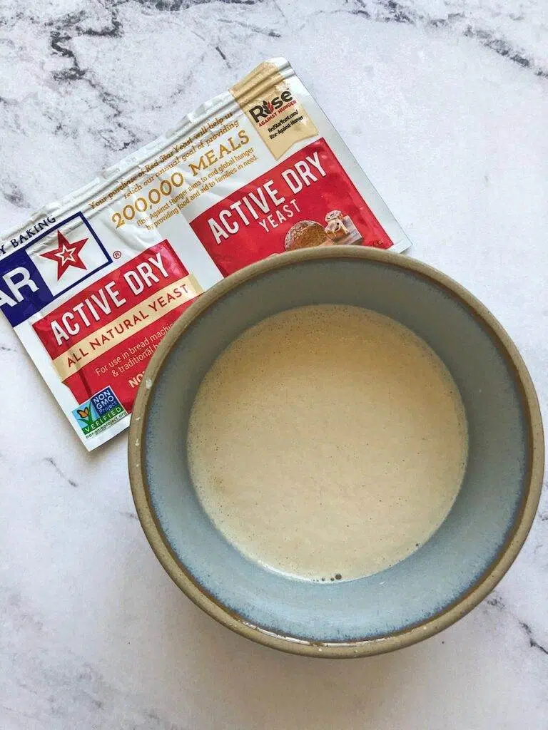A bowl of water with active dry yeast sprinkled in it, and the yeast package on the counter.