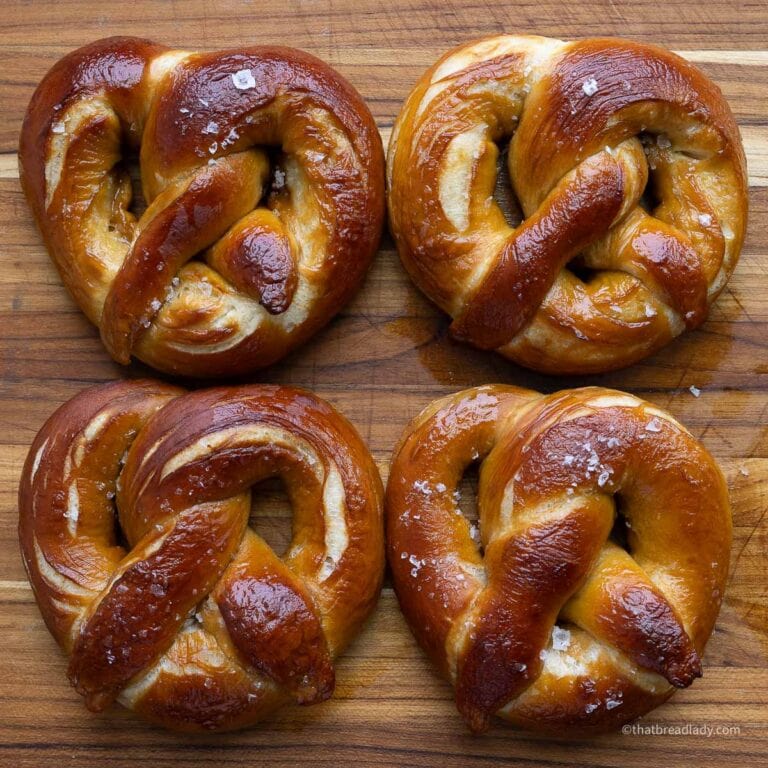 Four salted soft pretzels on a wood cutting board.