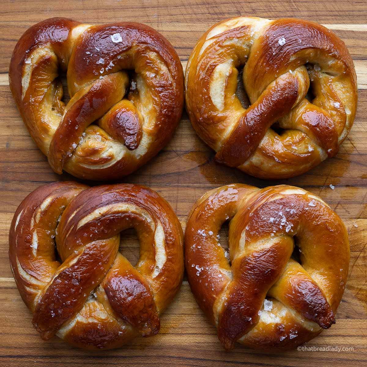 Four salted soft pretzels on a wood cutting board.