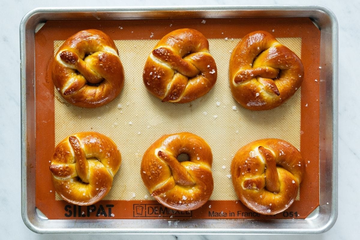 Six salted soft pretzels, on a baking sheet lined with a Silpat silicone mat.