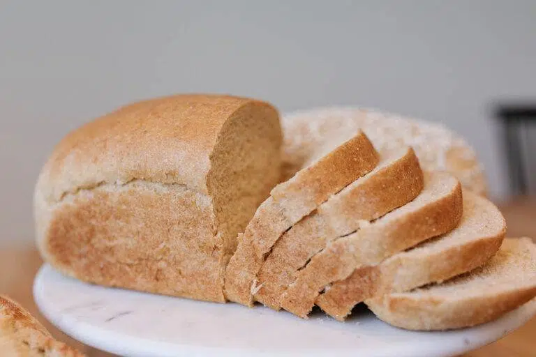 A loaf of whole wheat bread, half of it slices, on a cutting board.