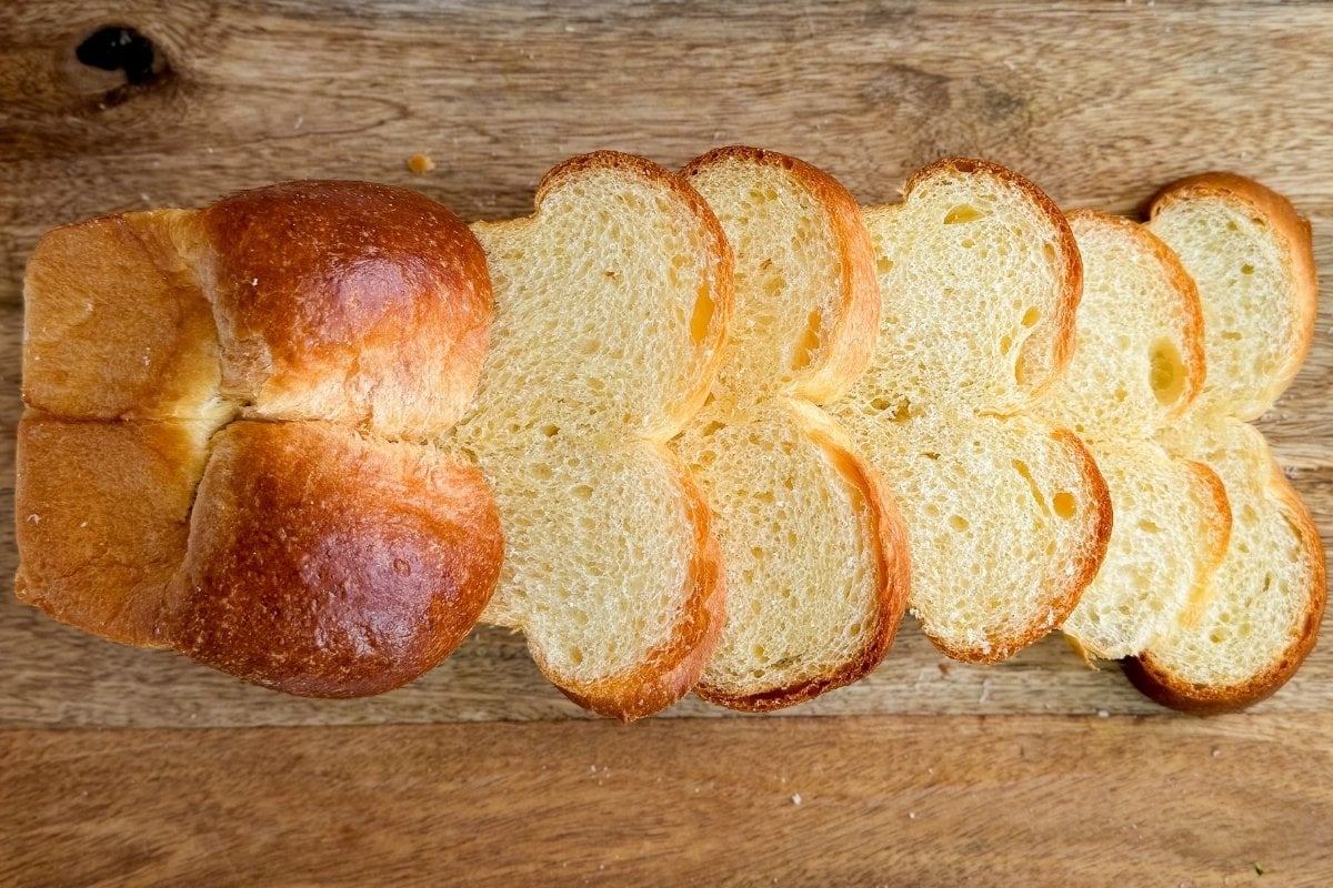A loaf of sliced brioche bread on a wood cutting board.