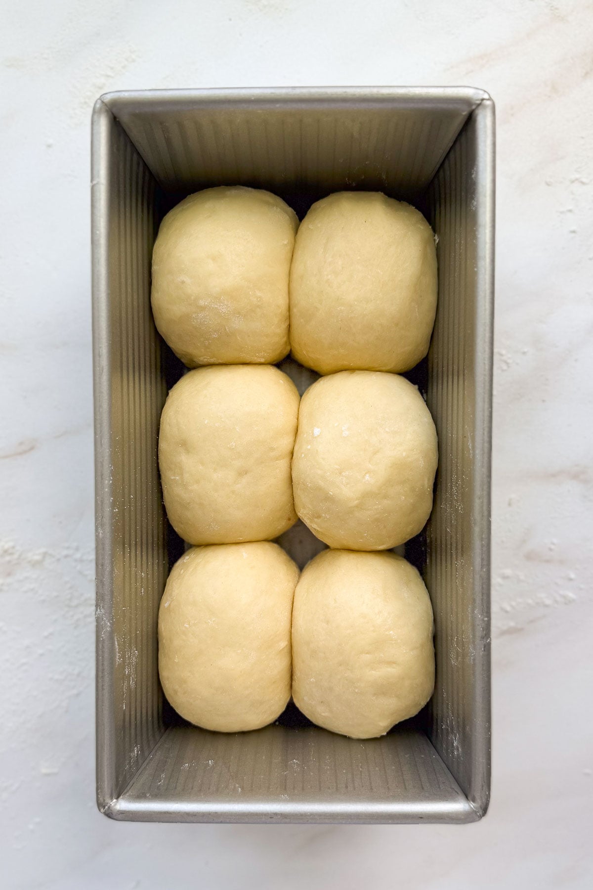 A loaf of unrisen french brioche bread in a metal bread pan.