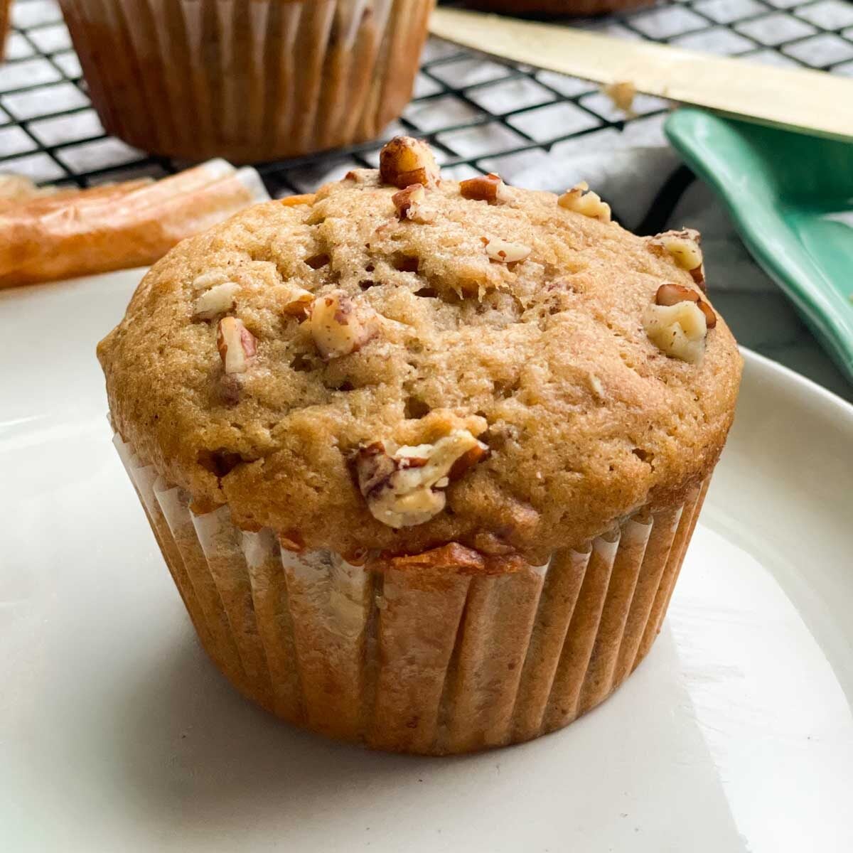 A pumpkin sourdough muffin with chopped pecans on top, resting on a plate.