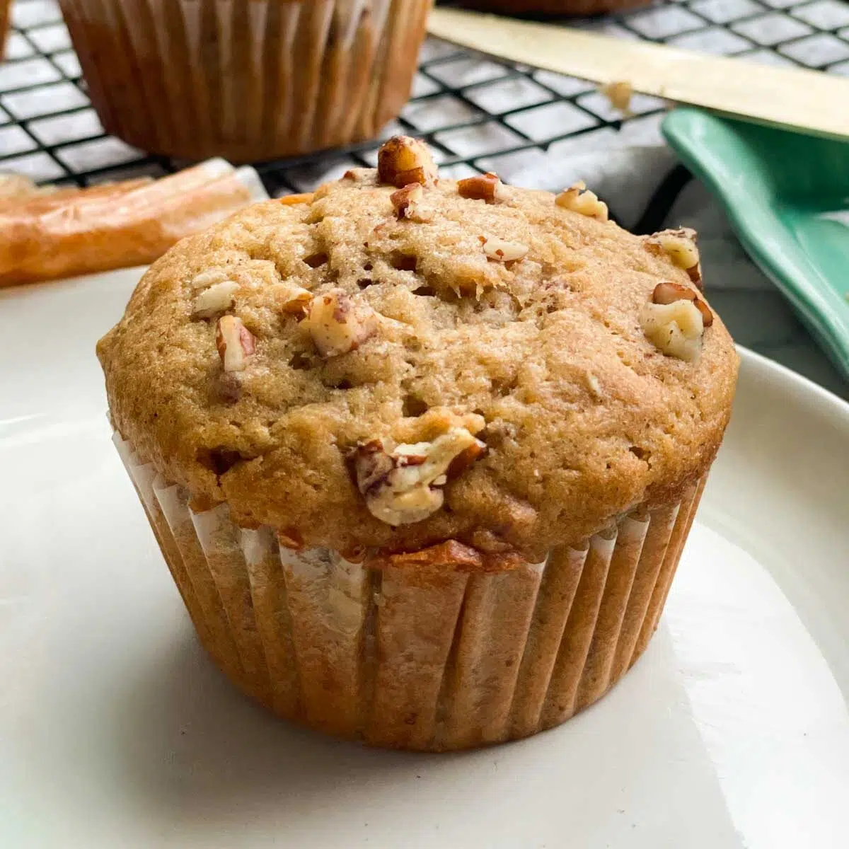 A pumpkin sourdough muffin with chopped pecans on top, resting on a plate.
