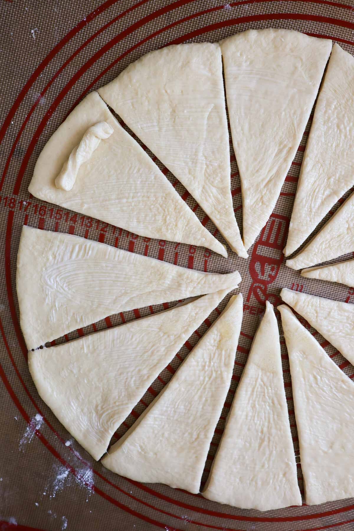 Crescent roll dough, rolled out to a circle, cut into 12 triangle wedges, with a small piece of dough resting on top of one of the wedges.