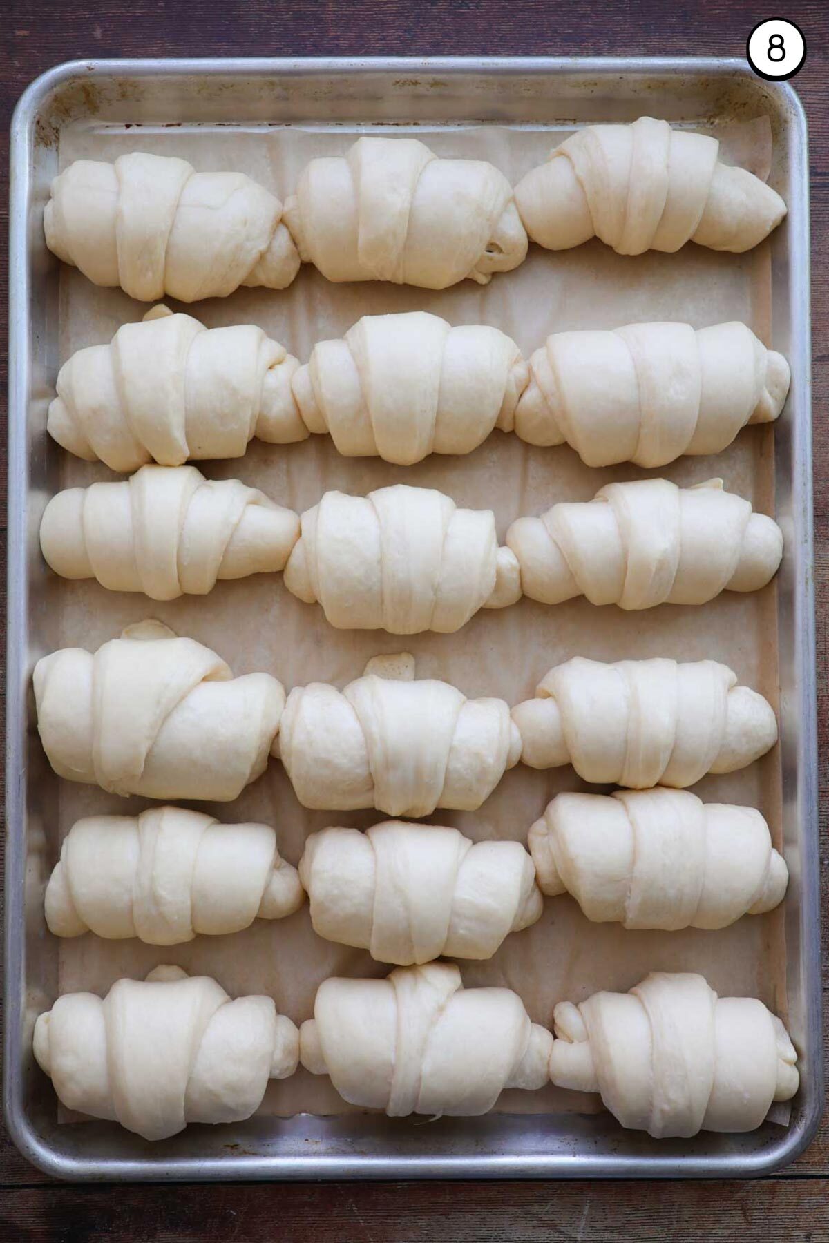 A sheet pan lined with parchment paper, and 18 risen, unbaked, crescent rolls on it with 6 rows of rolls and three rolls across.