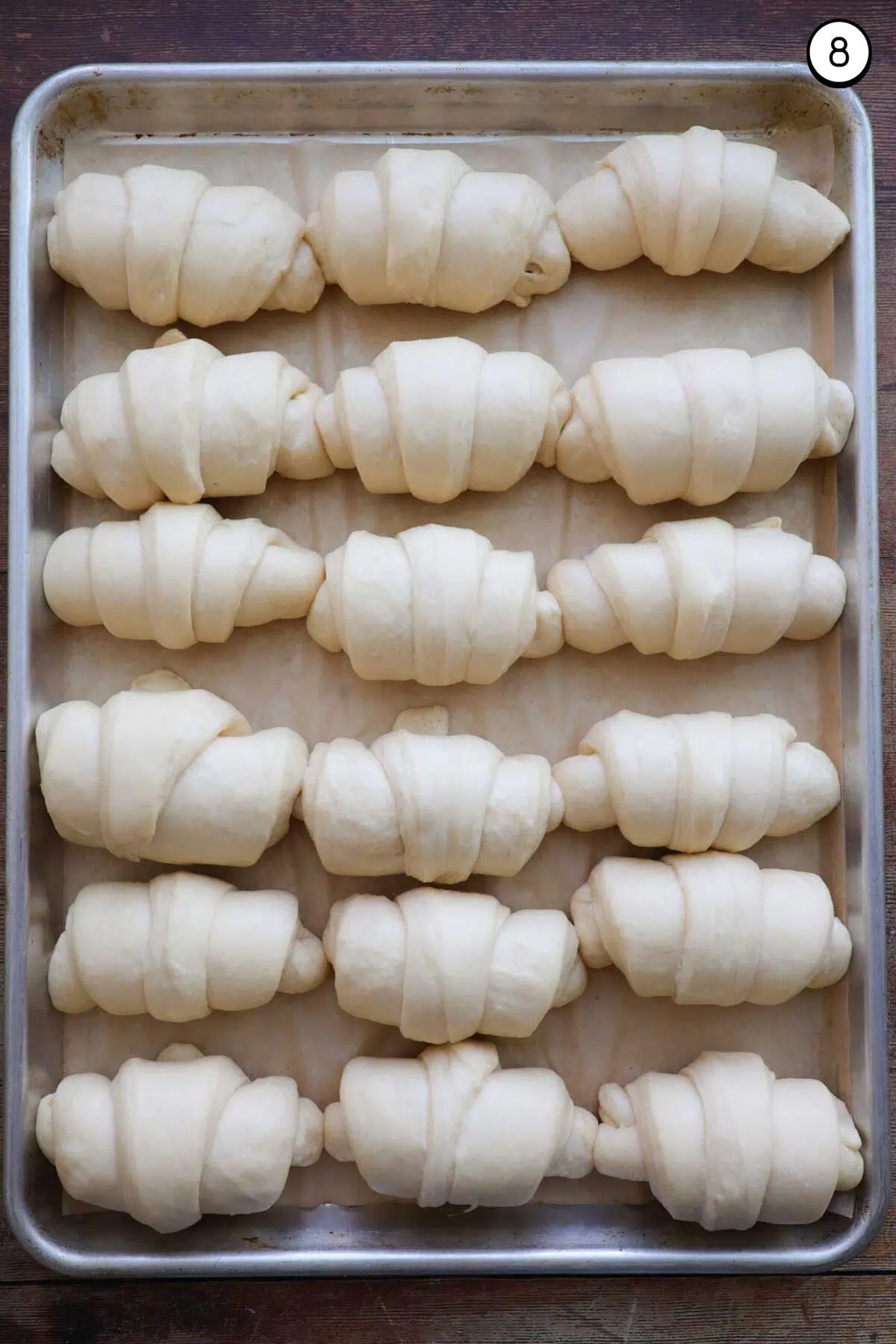 A sheet pan lined with parchment paper, and 18 risen, unbaked, crescent rolls on it with 6 rows of rolls and three rolls across.