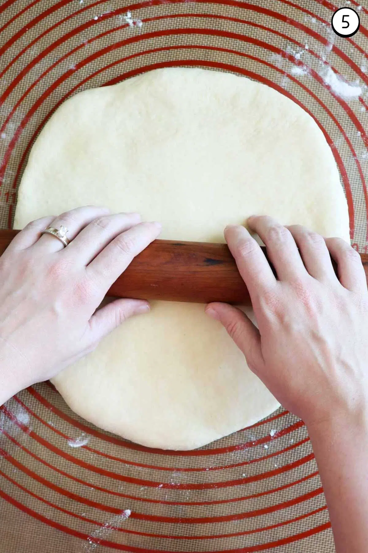 Two hands on a wood rolling pin, rolling out crescent roll dough on top of a silicone rolling mat.