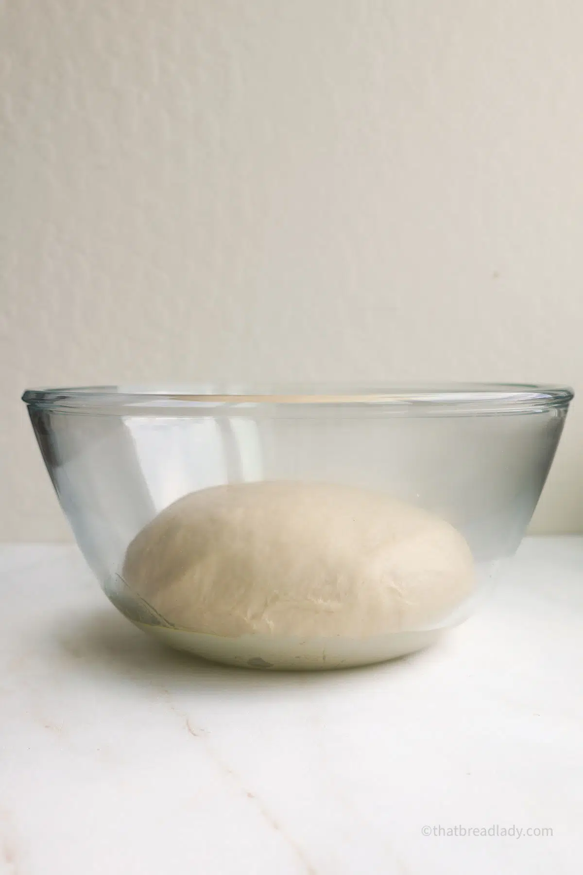 Dough in a glass bowl, on a countertop.