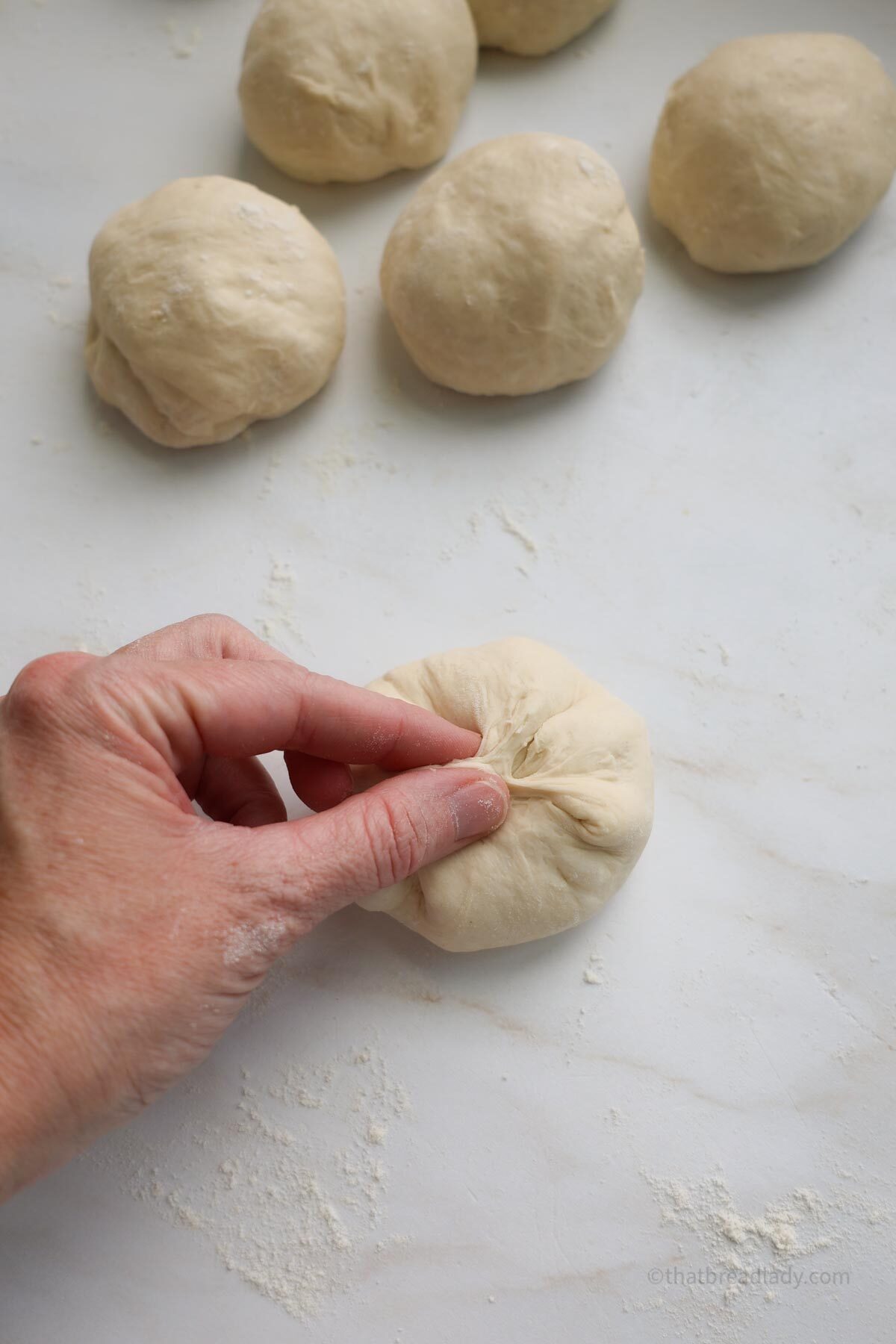 Fingers pinching dough together to form a small ball with 4 other dough balls on the counter beside it.