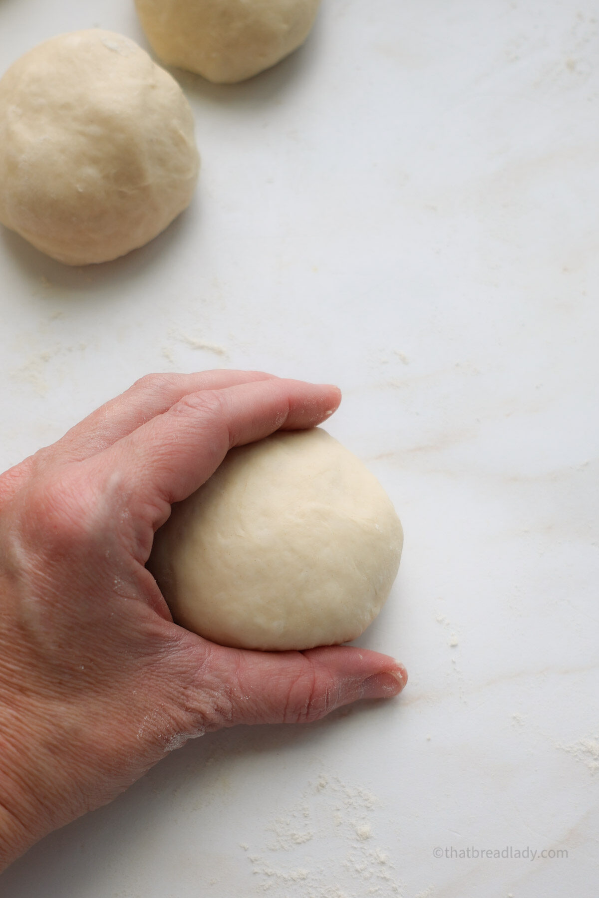 A hand cupping a dough ball with two other dough balls next to it.