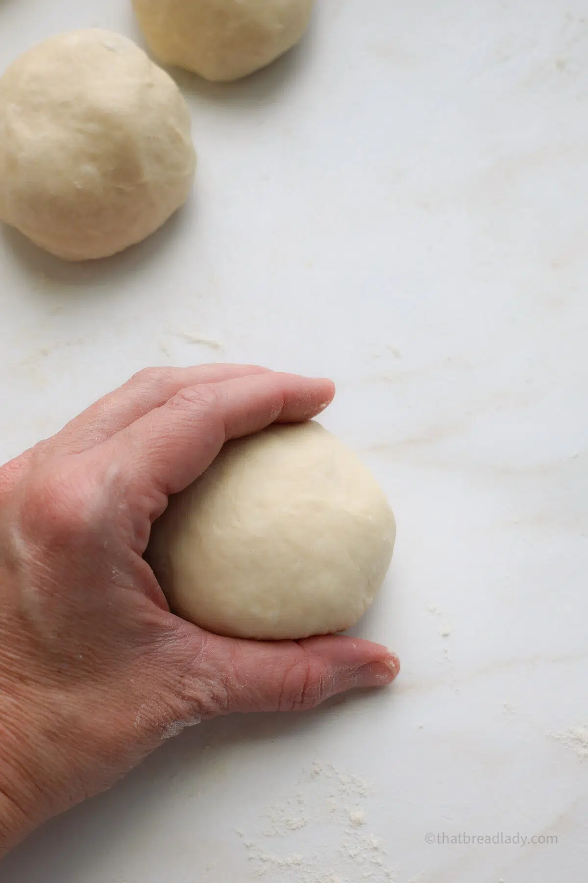 A hand cupping a dough ball with two other dough balls next to it.