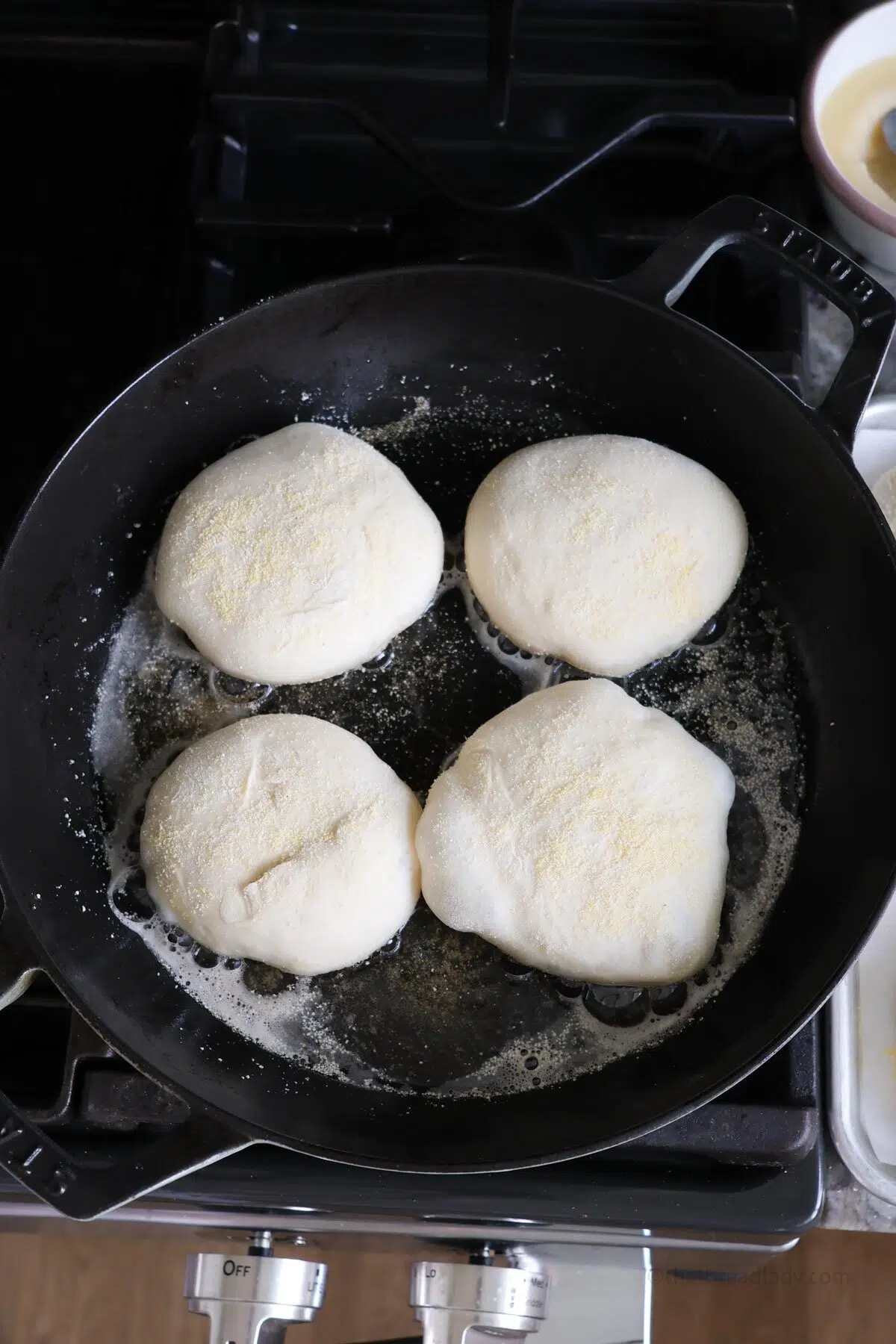 Four english muffins cooking in butter in a cast iron skillet on the stove top.