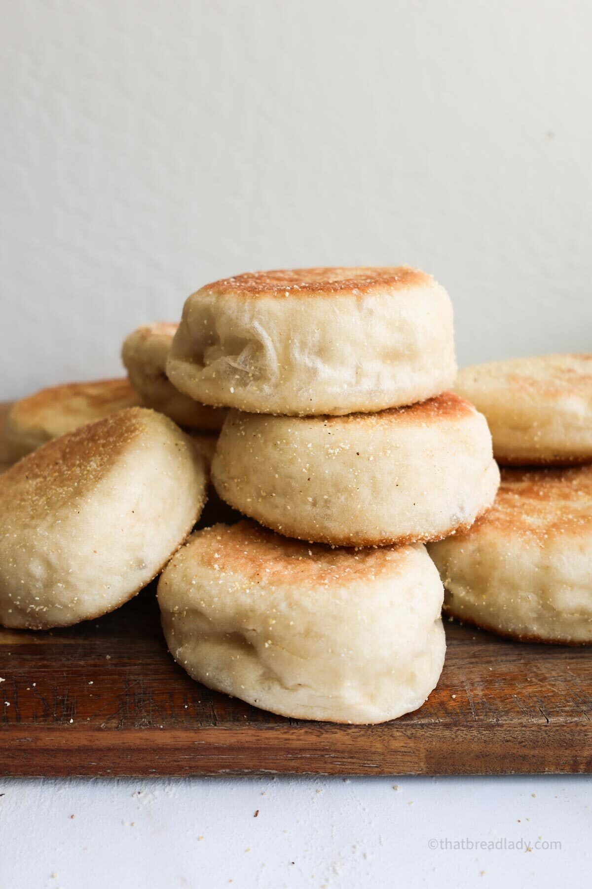 Sourdough English muffins stacked on top of a wood cutting board.