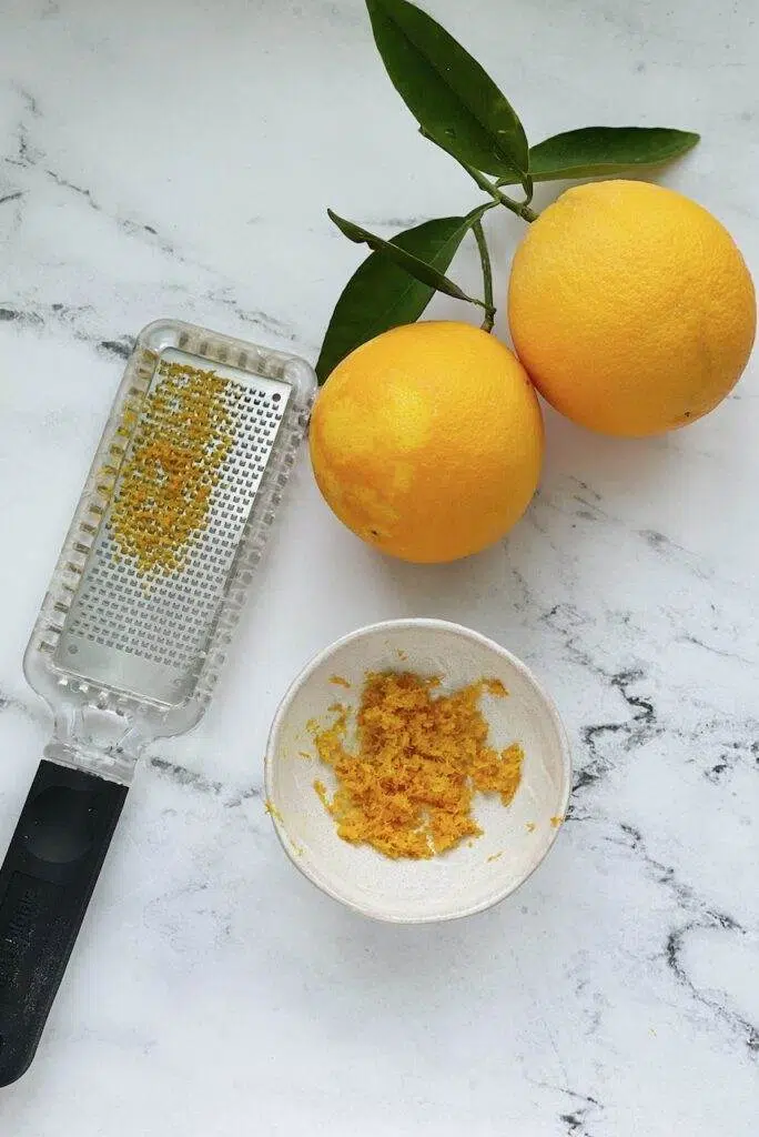 Oranges zested with zest in a bowl and a microplane with orange zested on it.