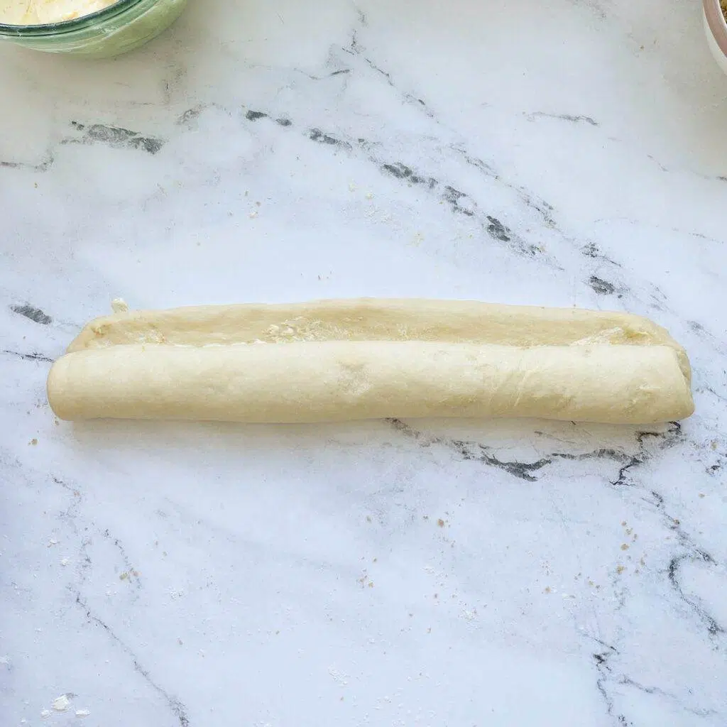 A piece of orange rolls dough rolled up into a log.