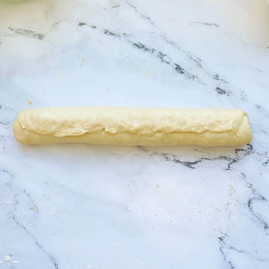 A piece of orange rolls rolled up into a log with the seam pinched shut.