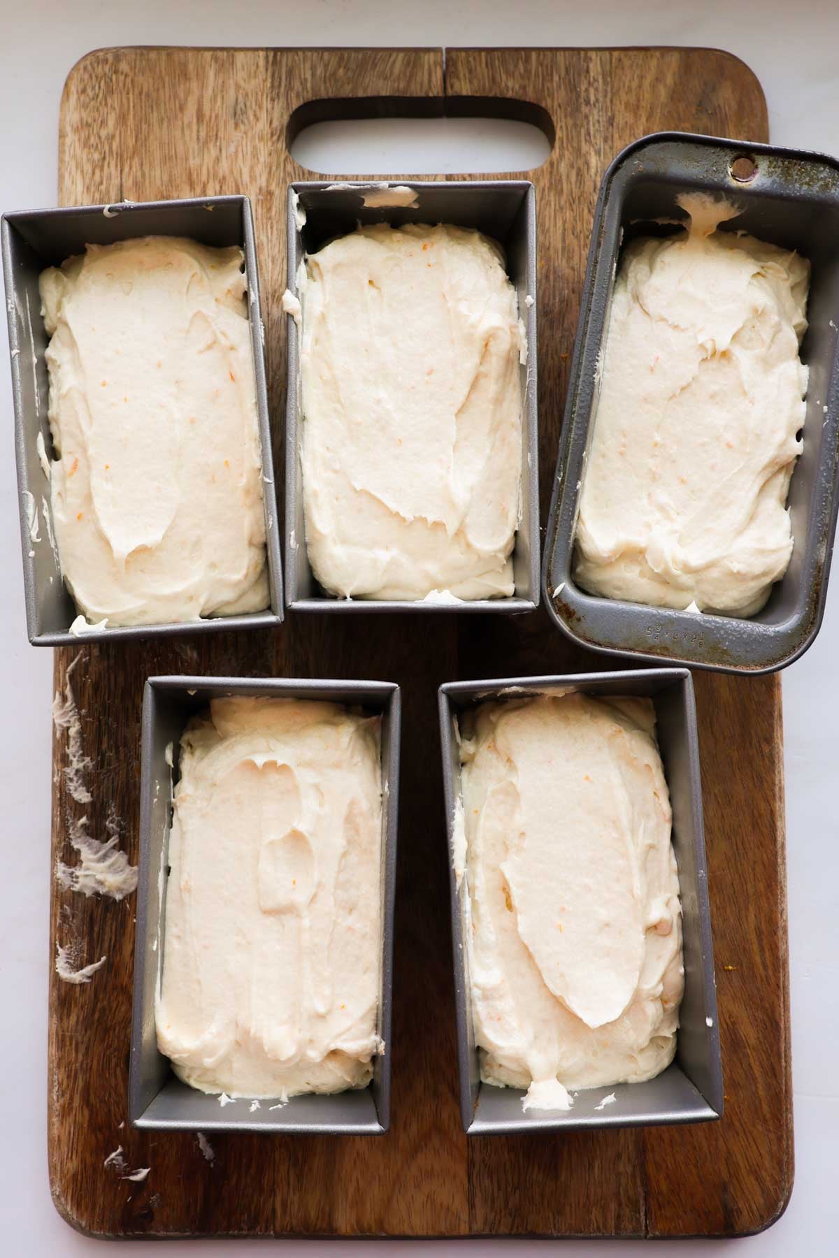 Five small pans, each filled about 2/3 full of orange pound cake batter.