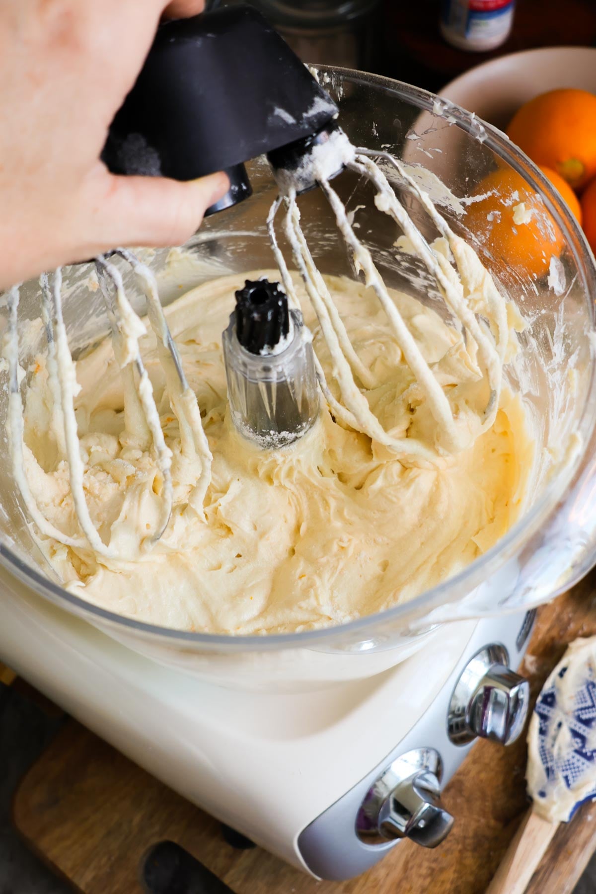 A stand mixer with the mixed ingredients for orange pound cake, and a hand removing the wire whisk attachment.