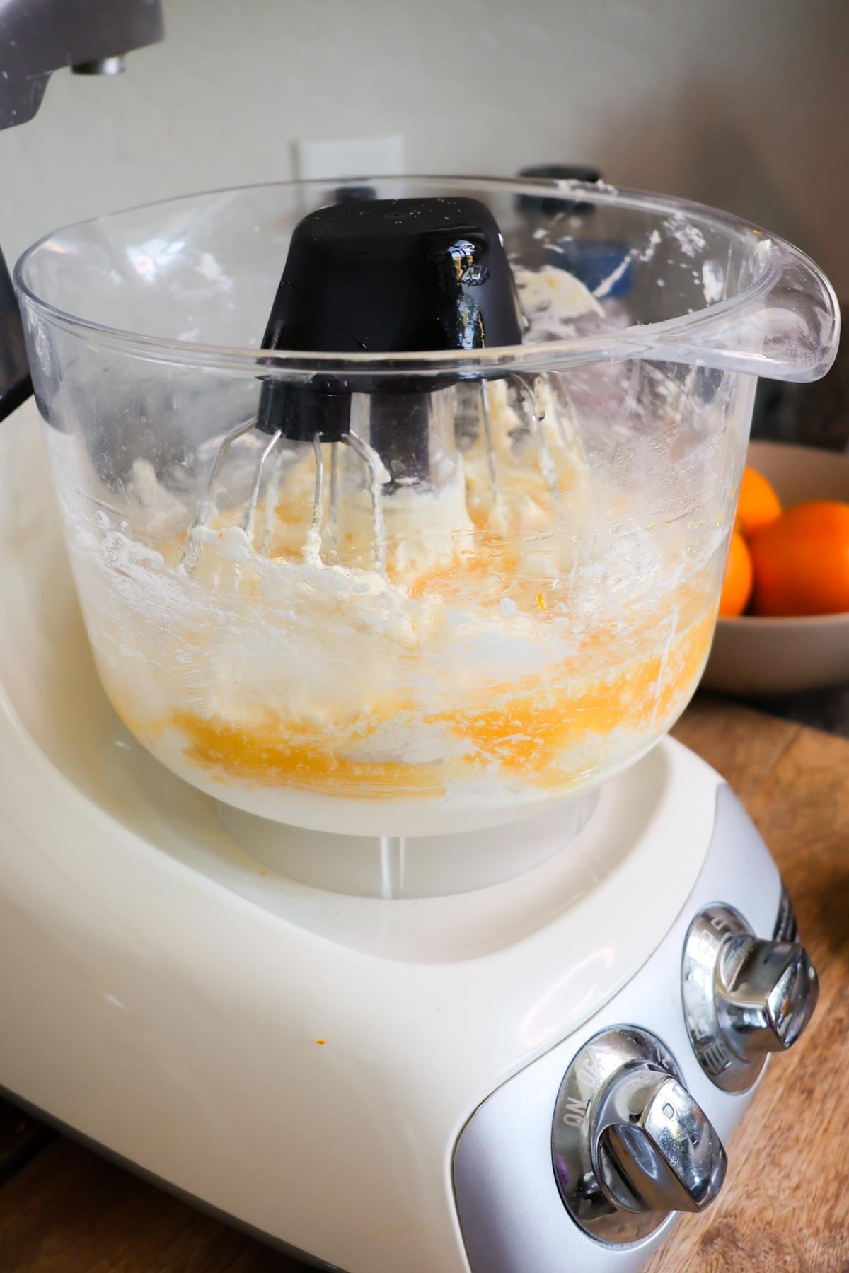 A stand mixer, with a bowl full of ingredients for orange pound cake, with eggs added on top.