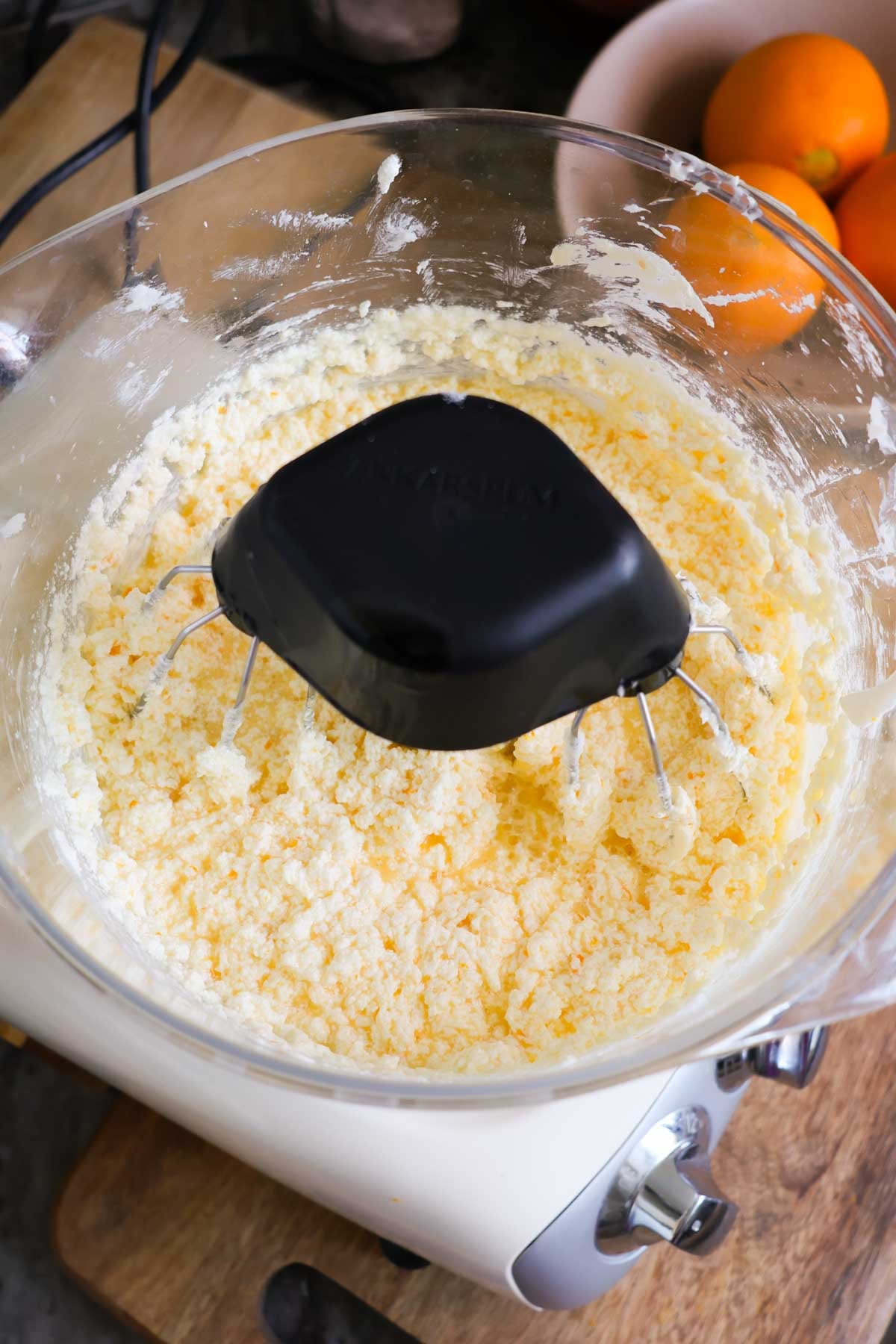 The bowl of a stand mixer, filled with ingredients of orange pound cake, with a chunky texture.