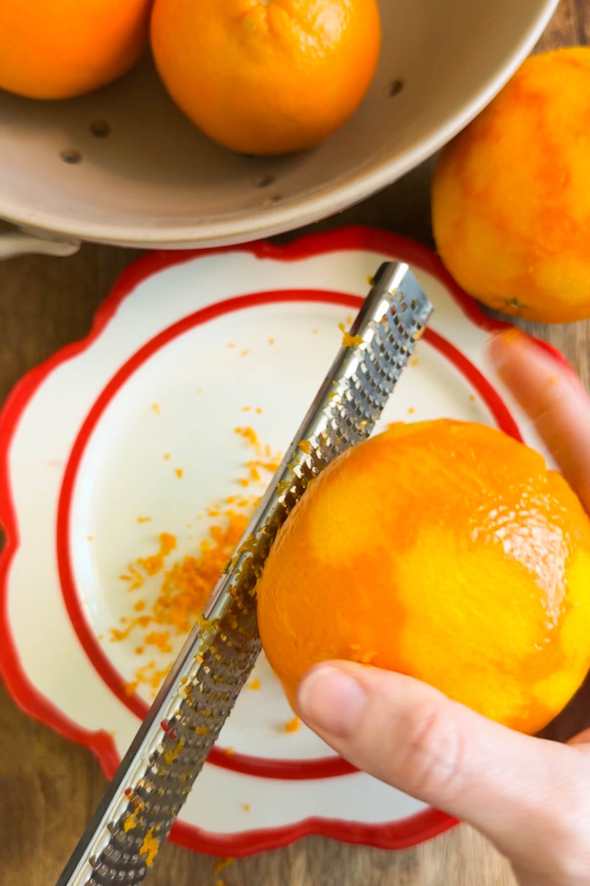 A hand holding an orange, zesting it with a citrus zester.