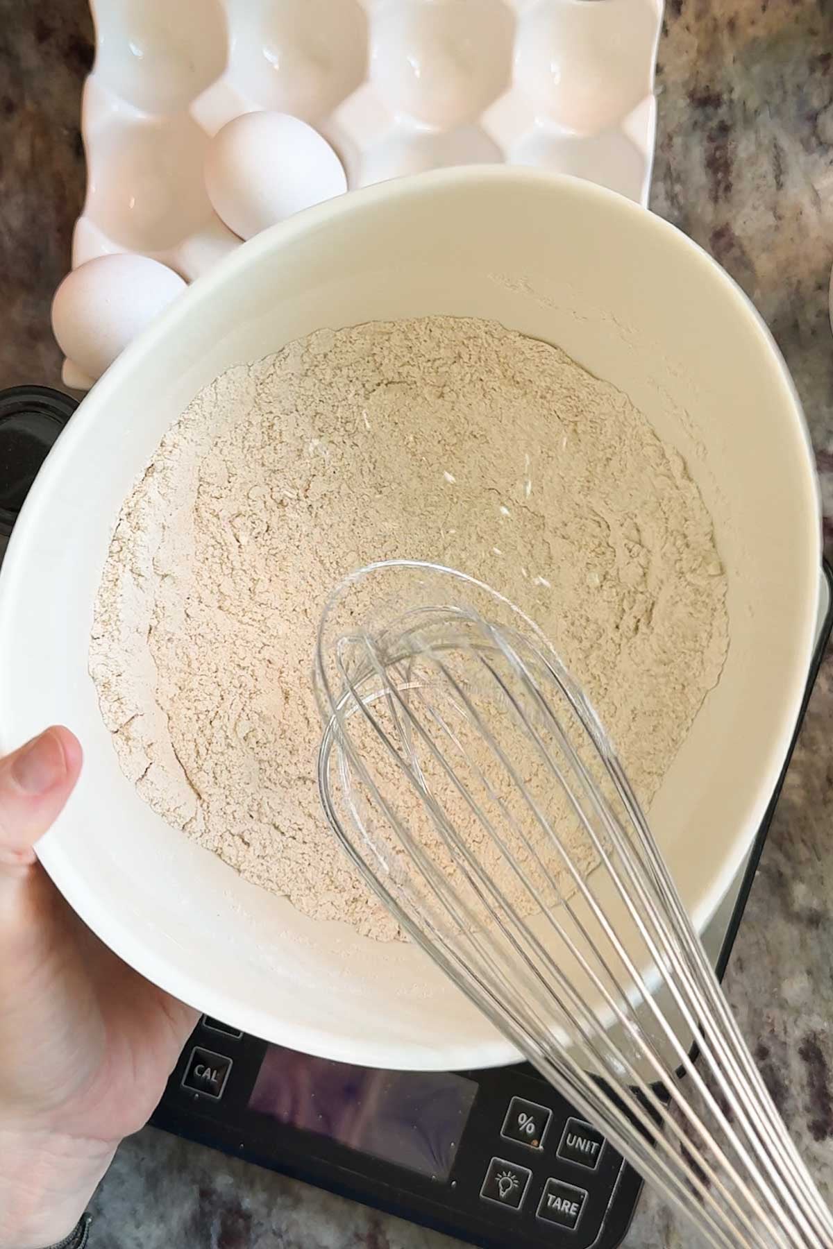 A bowl with a flour mixture and a wire whisk mixing it together.