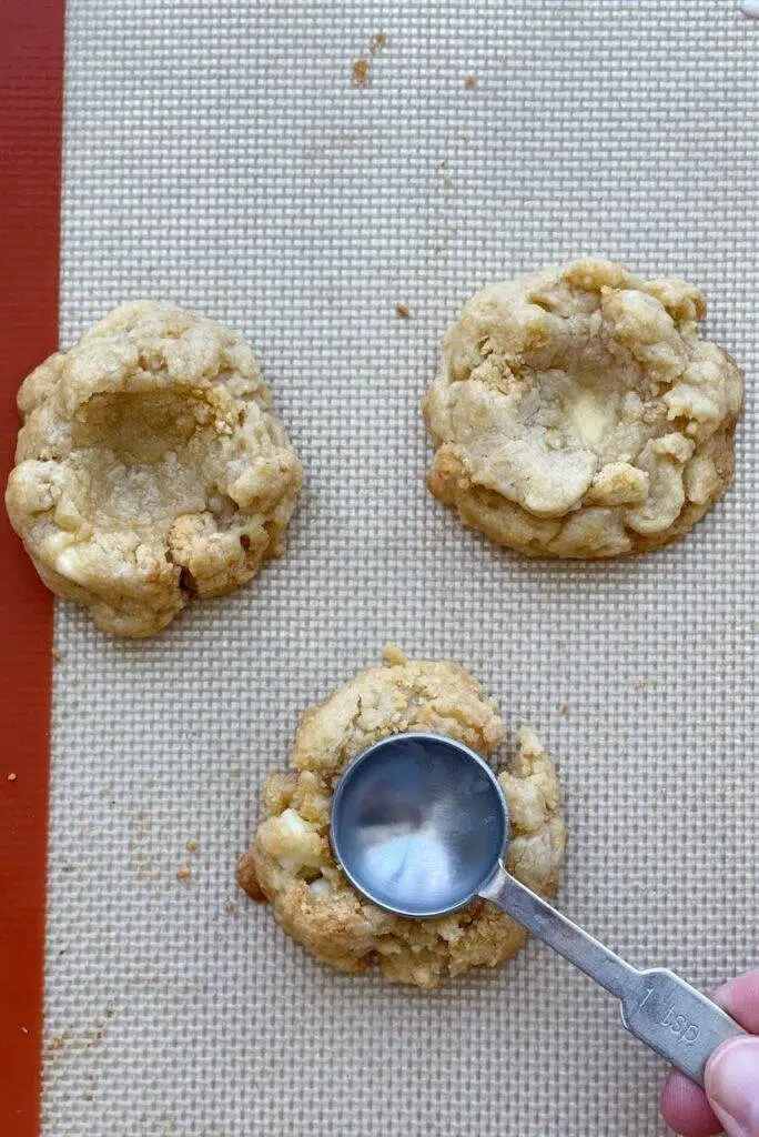 A spoon pressing down the center of a lemon cheesecake cookie, with two other cookies next to it.