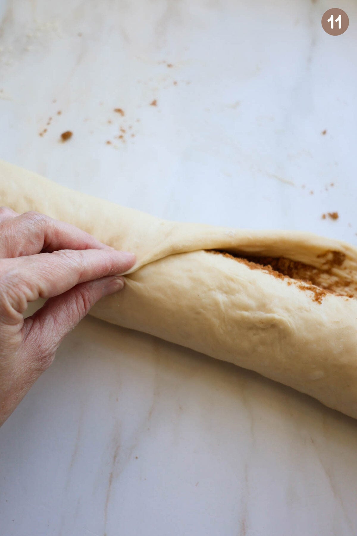 A hand pinching the edge of a cinnamon roll together with the roll of dough.