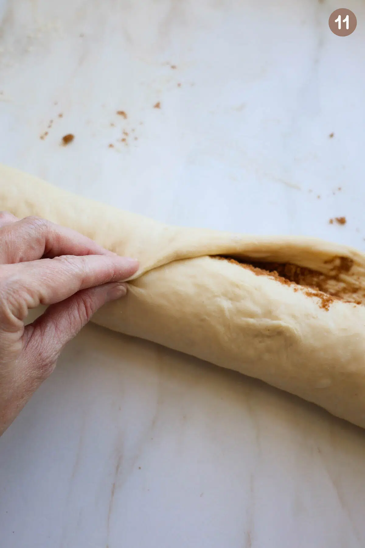 A hand pinching the edge of a cinnamon roll together with the roll of dough.