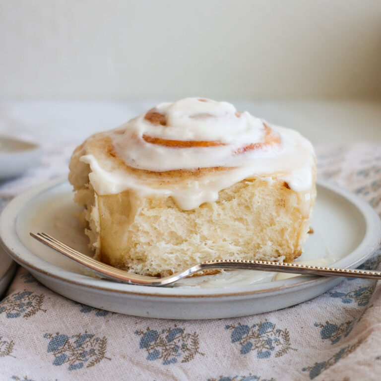 A homemade cinnamon roll with cream cheese icing on a plate with a fork.