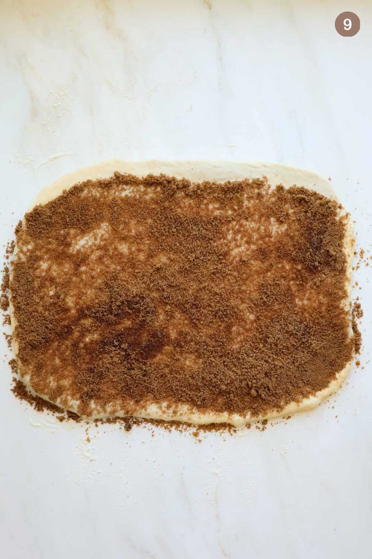 Cinnamon roll dough in a rectangular shape with brown sugar and cinnamon spread on top.