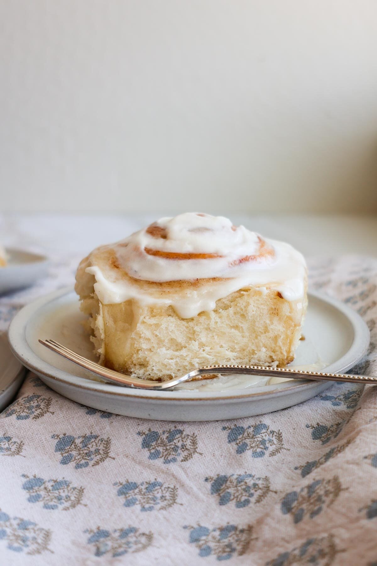 A cinnamon roll with icing on a plate with a fork.