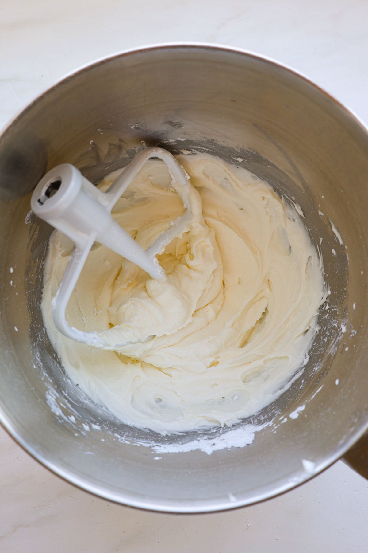 A mixing bowl with cream cheese frosting and a paddle attachment resting inside.