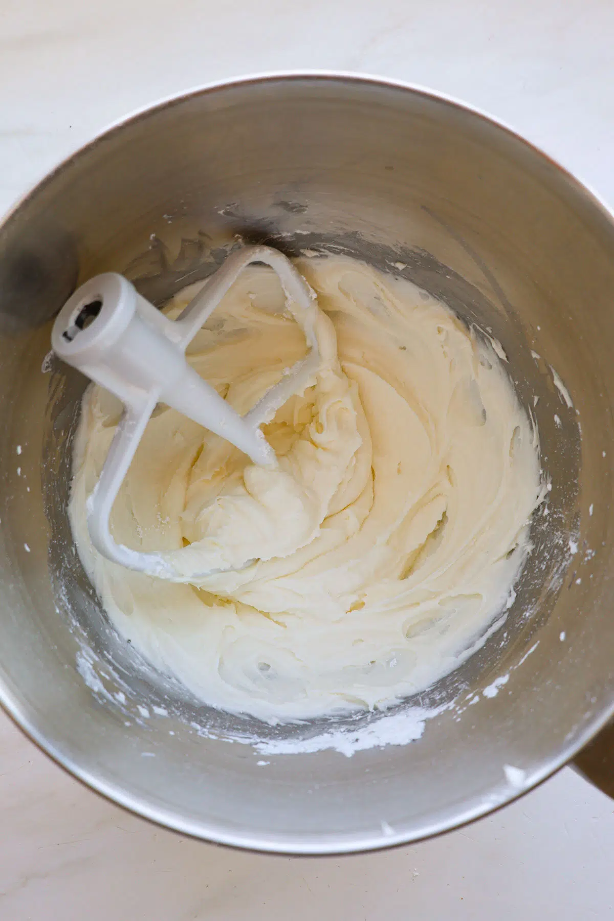 A mixing bowl with cream cheese frosting and a paddle attachment resting inside.