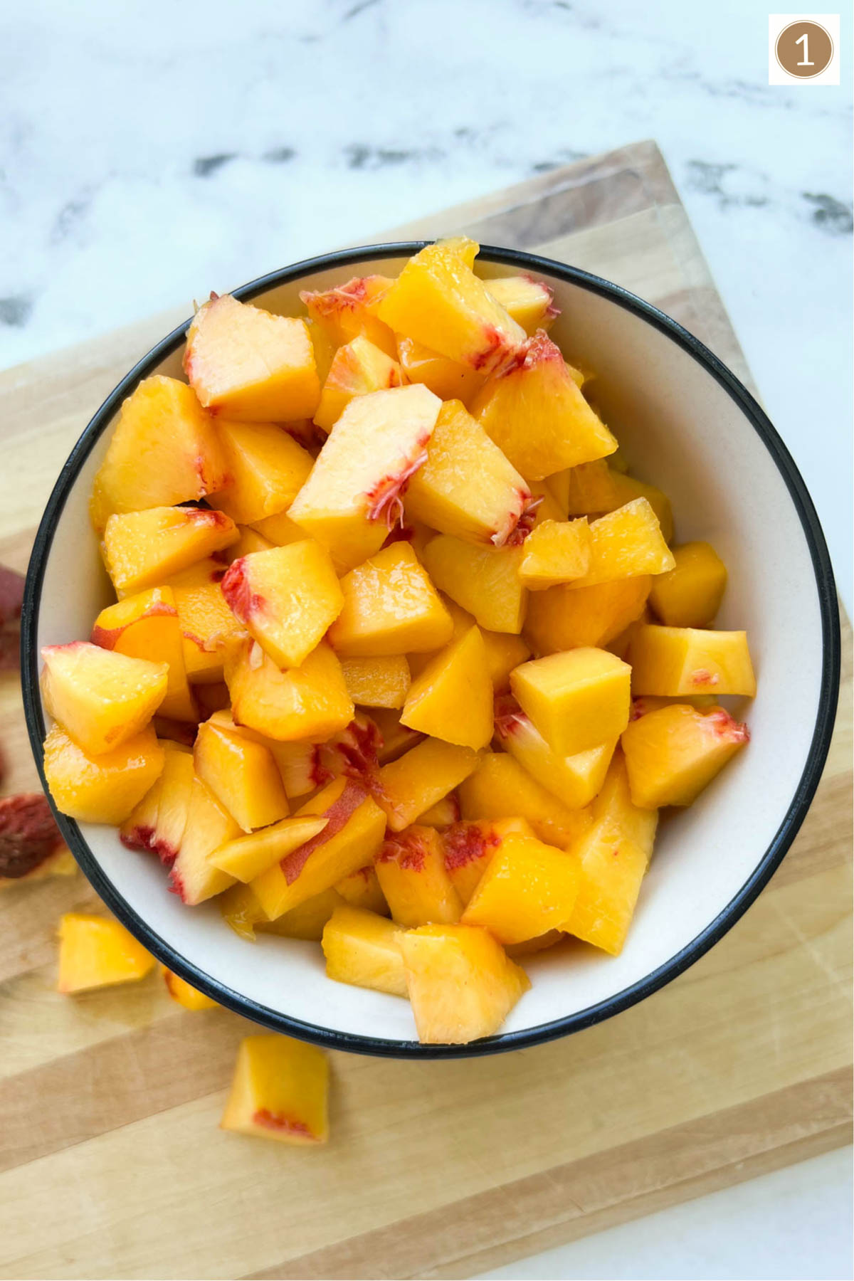 A bowl of chopped peaches on top of a wood cutting board.