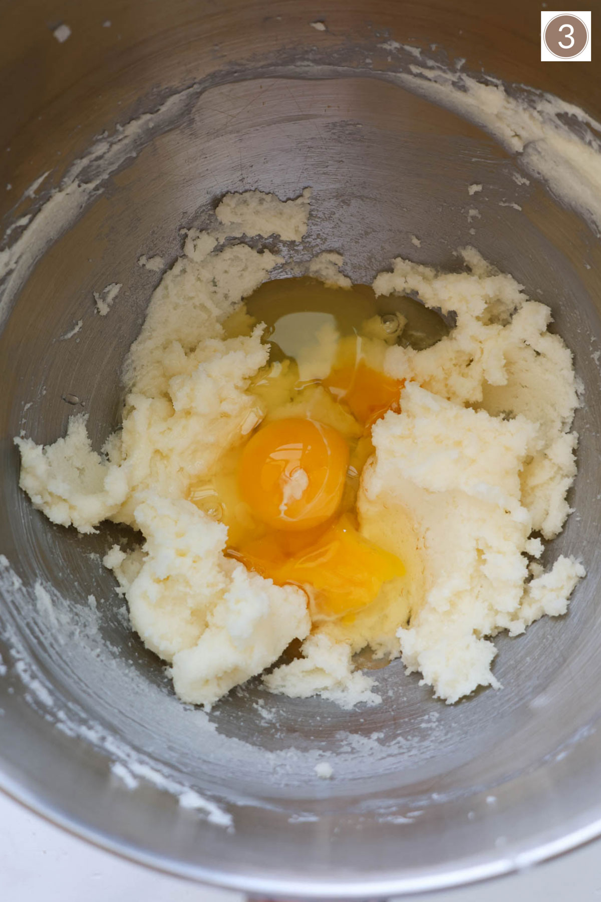 A silver mixer bowl with creamed sugar and butter and cracked eggs resting on top.