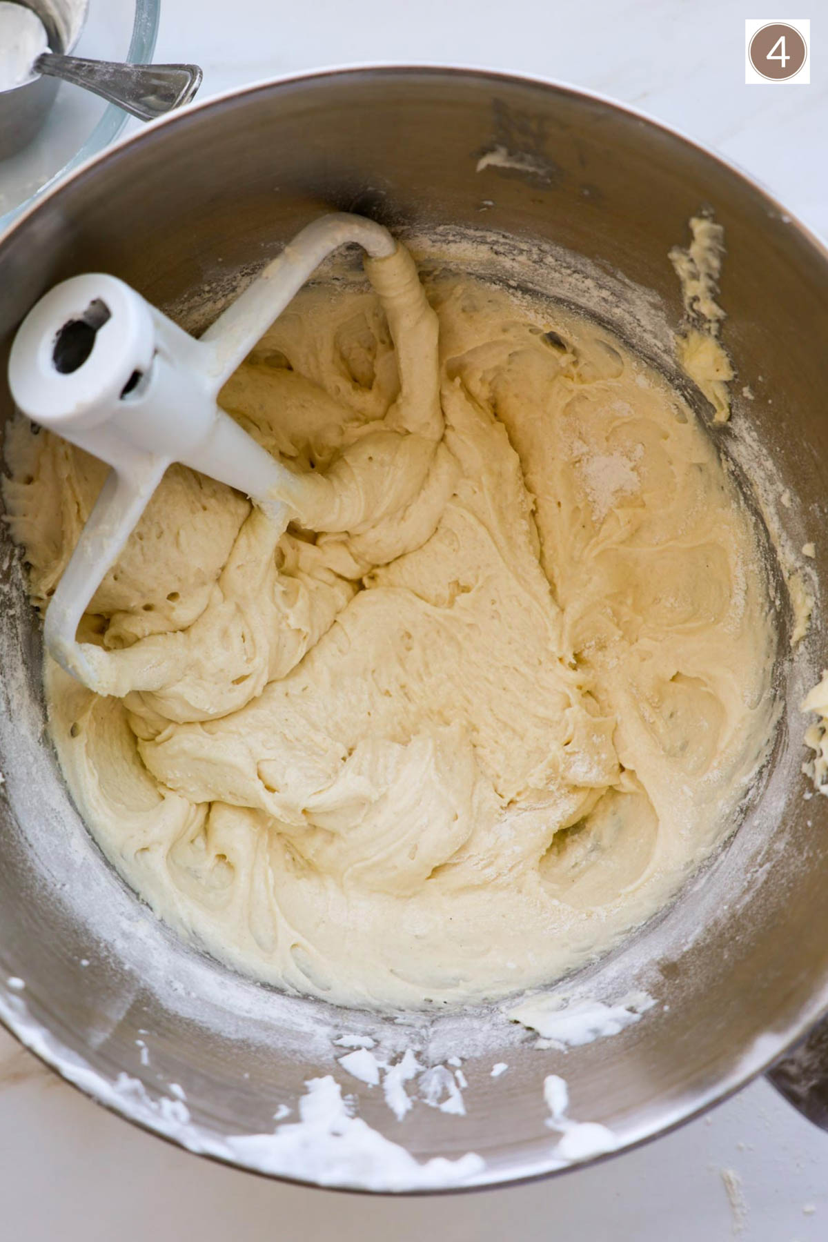 A sliver mixing bowl filled with sweet bread batter and a mixing paddle attachment on top.