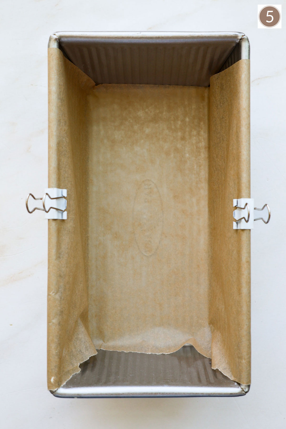 A bread pan lined with parchment paper held in place with two white clips.