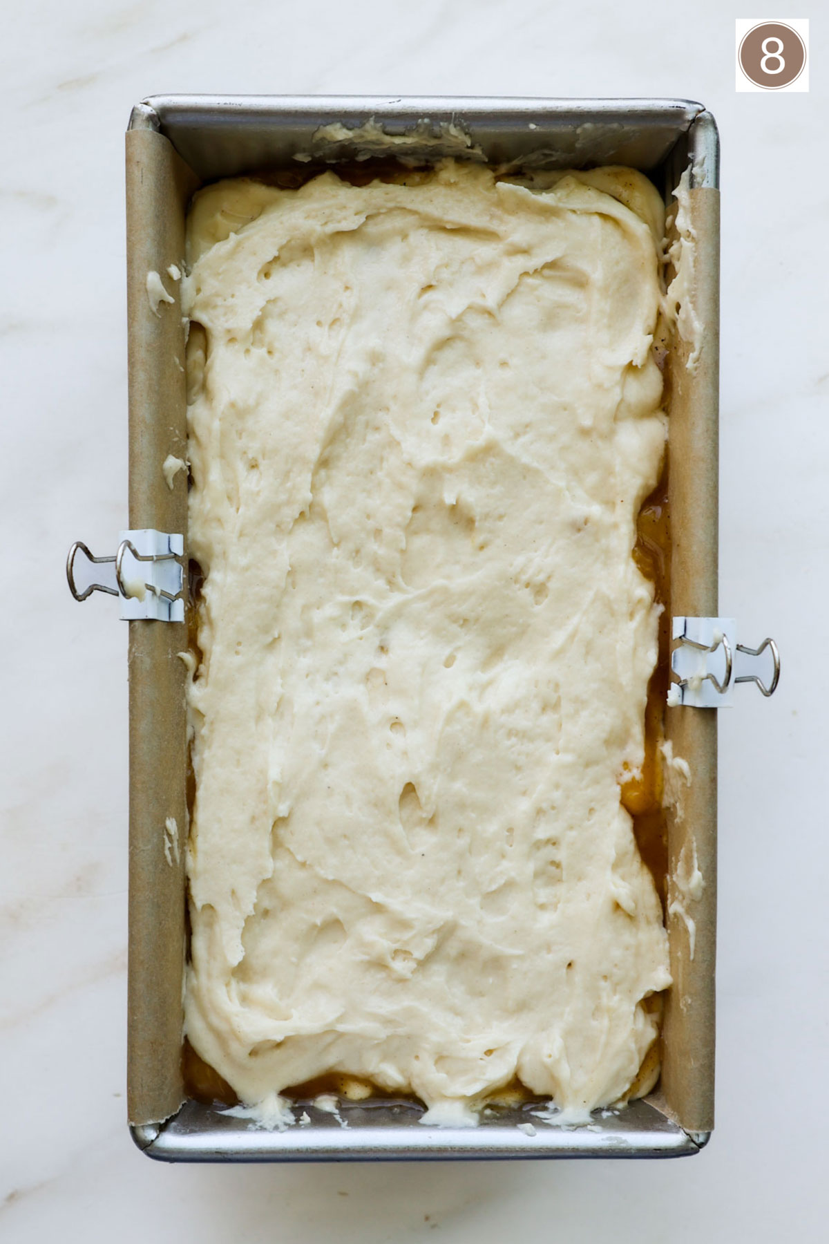 A bread pan lined with parchment paper held in place with two white clips and filled with bread batter.