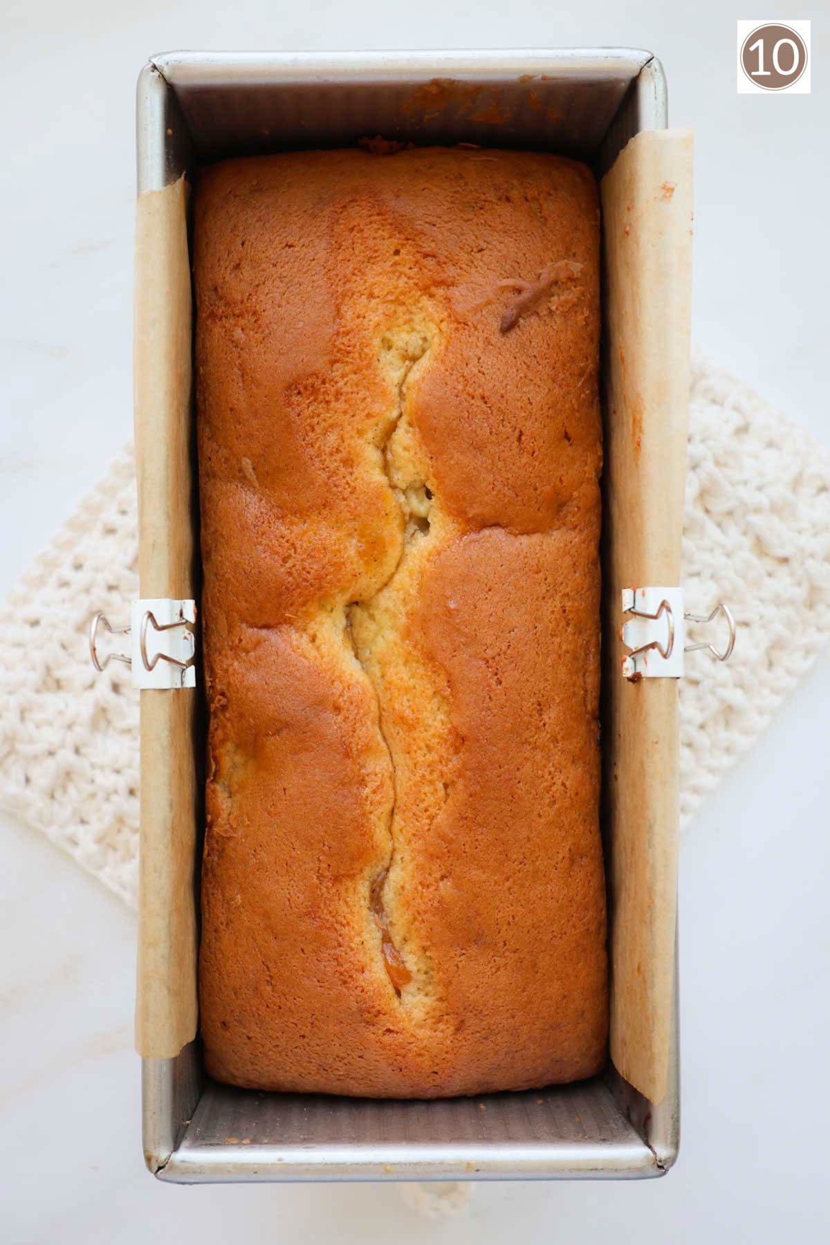 A baked loaf of peach bread in the pan cooling on a white crocheted hot pad.