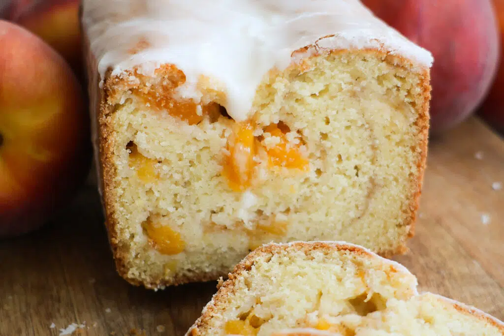 A cross-section of a loaf of peach bread and whole peaches on either side of it.