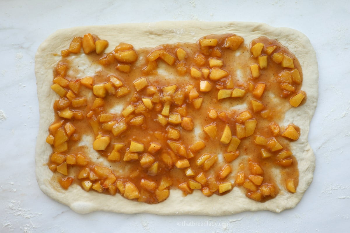 Rolled out dough topped with peach filling.