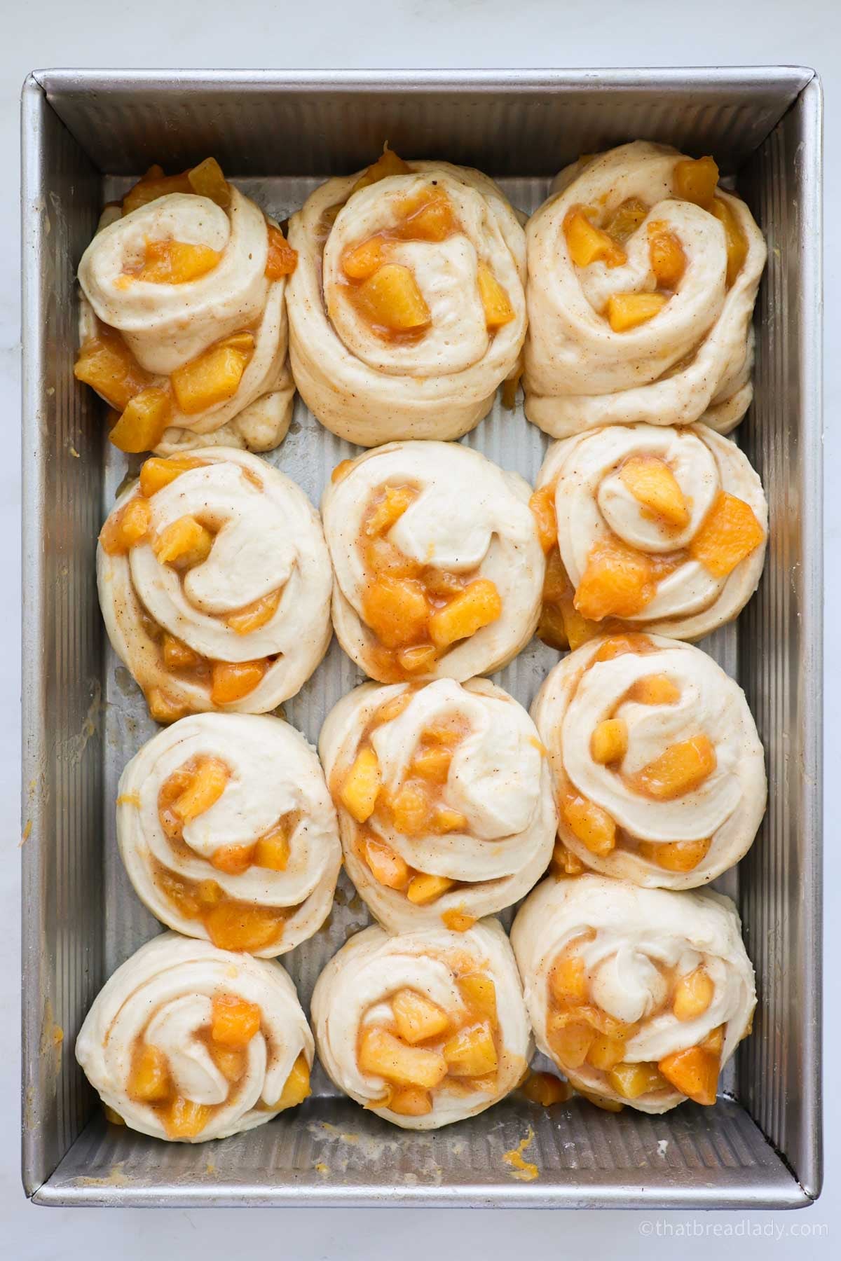 Peach cinnamon rolls rising in a metal cake pan.