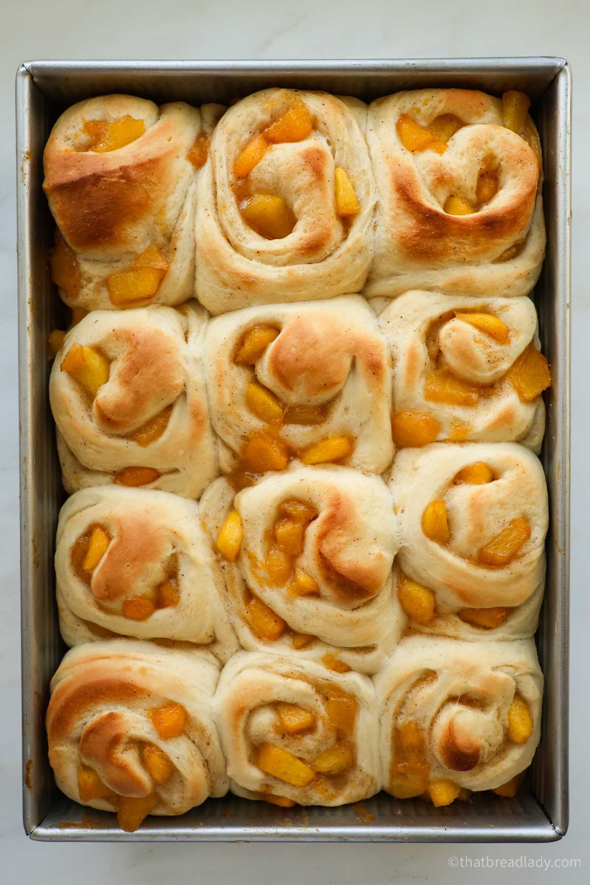 Baked, unfrosted peach cinnamon rolls in a metal cake pan.