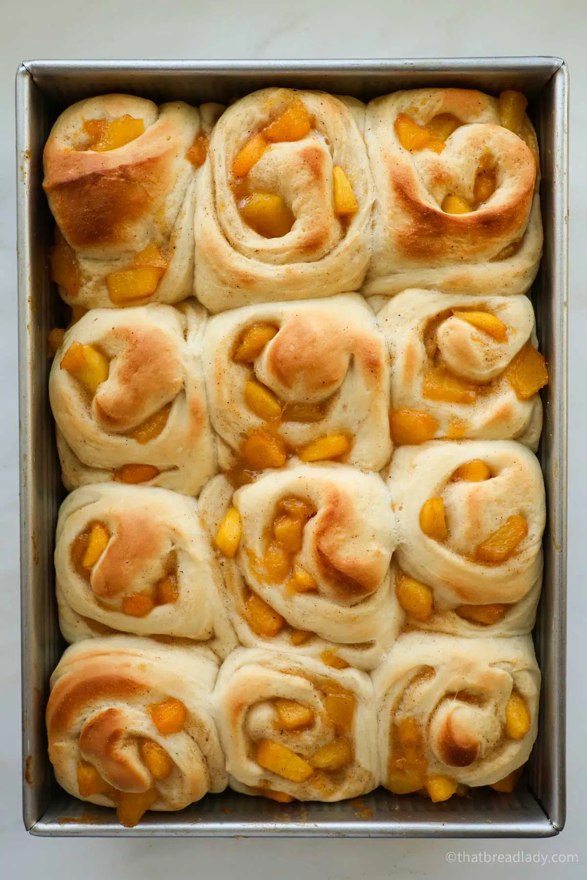 Baked, unfrosted peach cinnamon rolls in a metal cake pan.