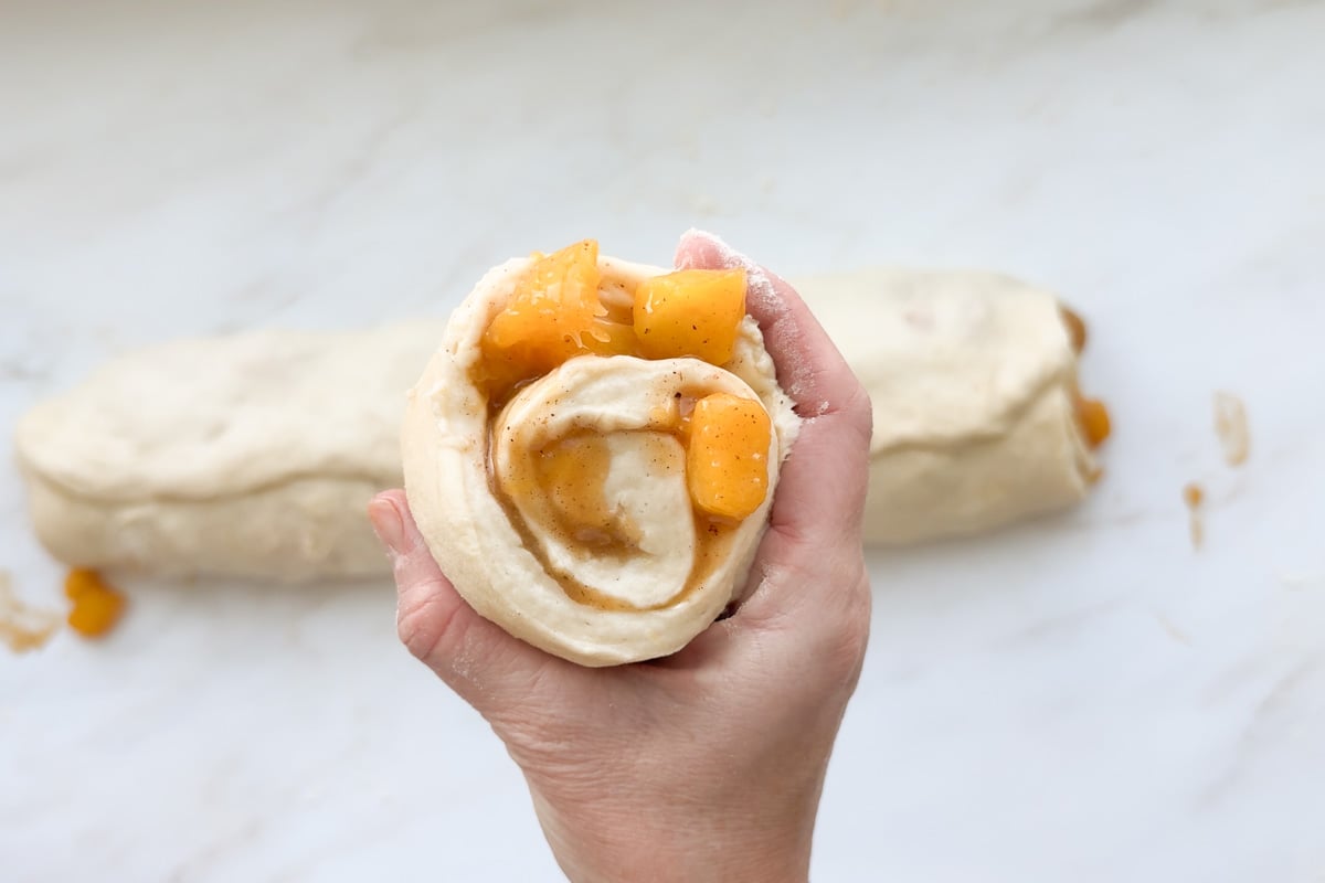 A cut peach cinnamon roll with peach chunks inside the swirl.