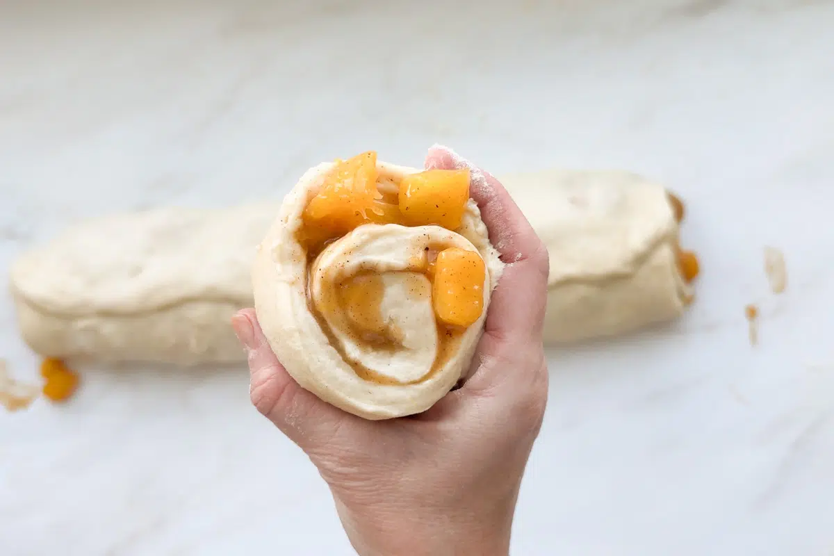 A cut peach cinnamon roll with peach chunks inside the swirl.