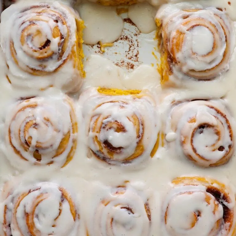 Pumpkin cinnamon rolls, frosted, in a pan, with one missing.